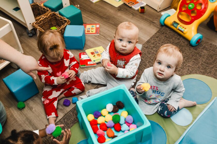 Three infants playing with clay on the floor.